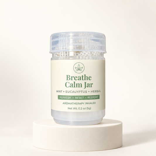 A clear plastic jar of Breathe Calm Jar aromatherapy inhaler with a cream-colored label and green text, displayed on a round white pedestal against a warm off-white background.